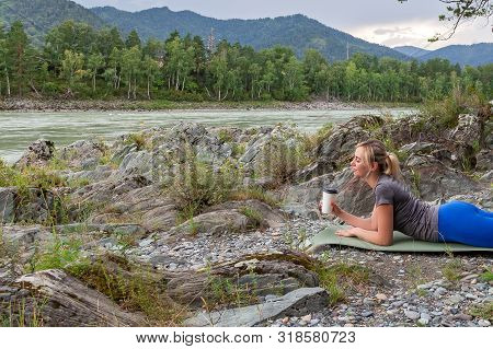 Blond Beautiful Girl Lying On The Mat On The Stone Ground Drinking Coffee Or Tea, Resting After Spor