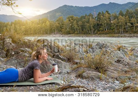 Blond Beautiful Girl Lying On The Mat On The Stone Ground Drinking Coffee Or Tea, Resting After Spor