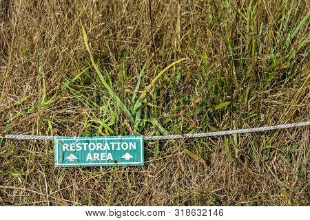 Natural grassland restoration green and white information sign with rope on ground.