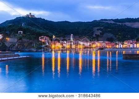 Reflection In The Blue Water Of Dawn Of The Village Of Colliure With Mountain And Castle, France