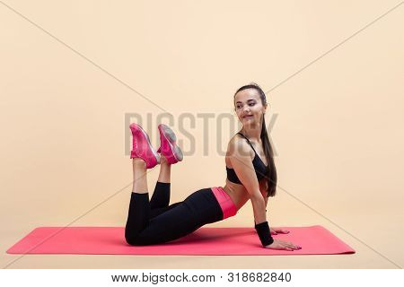 A Young Attractive Girl With A Ponytail, A Brunette, Is Lies In A Cobra Pose With Knees Bent, Doing 