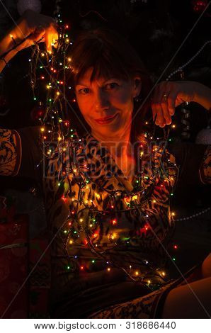 Close-up Portrait Of An Adult Beautiful Brunette Woman Near A Christmas Tree Holding A Bright Christ