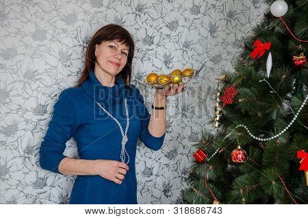 Older Adult Beautiful Brunette Woman In A Casual Style Hanging Balls Decorates A Christmas Tree And 