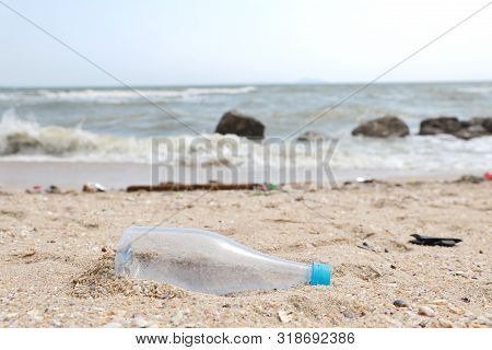 Close Up Image Of Empty Plastic Water Bottle On Dirty Beach Filled With Plastic Pollution, Garbage A