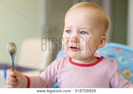 Cute Adorable Caucasian Blond Toddler Boy Sitting In High Chair And Crying While Feeding. Upset Unha
