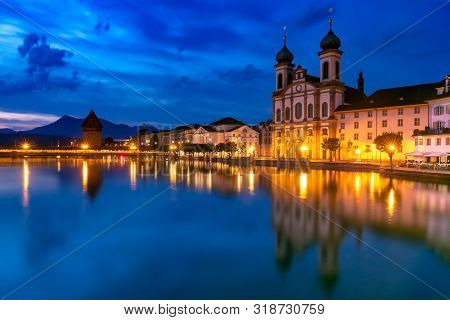 Jesuit Church And Water Tower, Wasserturm Along The River Reuss At Night In Old Town Of Lucerne, Swi