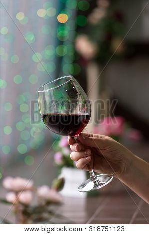 Hand Sommelier Holding Glass Of Red Wine. Glass Of Red Wine On Background Of Colorful Bar. Bokeh. Co