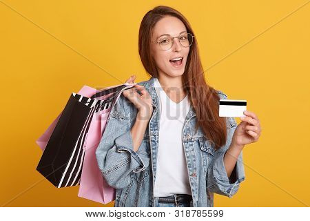 Indoor Photo Of Beautiful Smiling Caucasian Woman With Shopping Bags In Hands And Shows Credit Card,