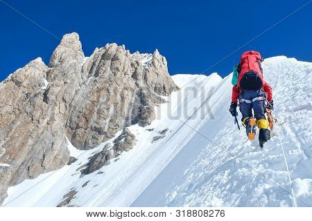Climber Reaches The Summit Of Mountain Peak Enjoying The Landscape View.