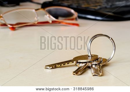 Set Of Three House Keys On The Ring On Table Near Glasses And Keyboard. Bunch Of Apartment Keys Clos