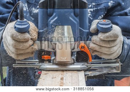 Man In Working Gloves Cuts A Plywood Plate Edge Using A Blue Electric Milling Cutter Tool With Orang