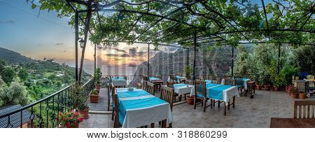 Sunset In The Distance Over The Ocean With Mountains And Dinner Tables And Trees