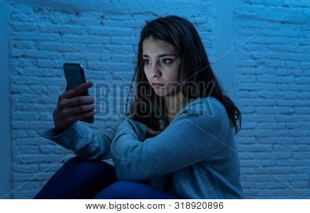 Portrait Of Sad Scared Young Woman On The Floor At Night Stressed And Worried On Smart Mobile Phone 