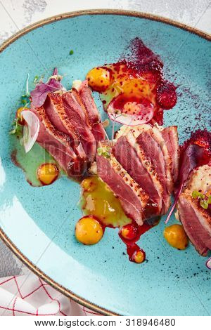 Sliced duck breast with hummus and plum sauce on turquoise plate top view. Exquisite serving restaurant main course with grilled goose fillet steak, greens and spices
