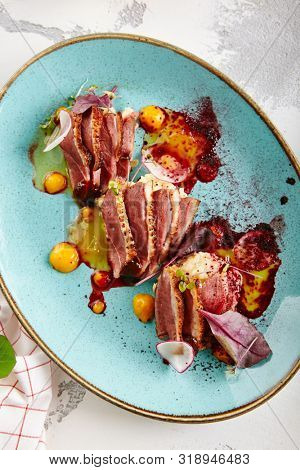 Sliced duck breast with hummus and plum sauce on turquoise plate top view. Exquisite serving restaurant main course with grilled goose fillet steak, greens and spices