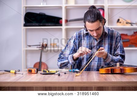 Young handsome repairman repairing violin