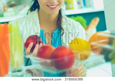 Portrait of female standing near open fridge full of healthy food, vegetables and fruits. Portrait of female