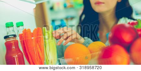 Portrait of female standing near open fridge full of healthy food, vegetables and fruits. Portrait of female