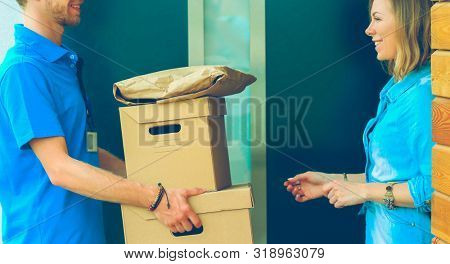 Smiling delivery man in blue uniform delivering parcel box to recipient - courier service concept