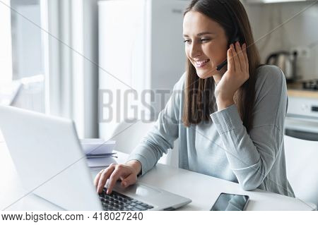 Smiling Young Female Employee Wearing Wireless Headset, Looking At Laptop Screen, Cheerful Woman In 