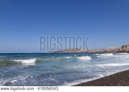 Coast And Beach Of Vlychada On Santorini Island In Greece. In The Background Blue Sky And Waves At S