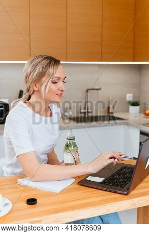 Blonde Girl With Laptop Drinking Majito Lemonade, Doing Homework In A Bright Kitchen. Education And 