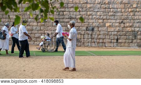 Anuradhapura, Sri Lanka - 03 31 2021: Old Lady In A Wheelchair With Flower Offerings And Her Son Tak