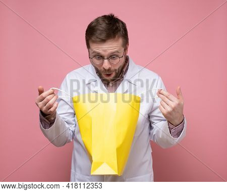 Doctor Received A Gift, He Holds A Yellow Package In Hands, Happily Looks Into It And Is Surprised. 
