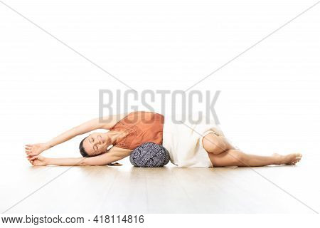 Restorative Yoga With A Bolster. Young Sporty Attractive Woman In Bright White Yoga Studio, Lying On