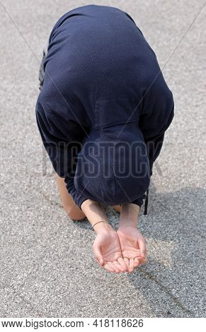 Very Poor Young Beggar Begs For Alms Kneeling In The Middle Of The Asphalt Road Of The Metropolis