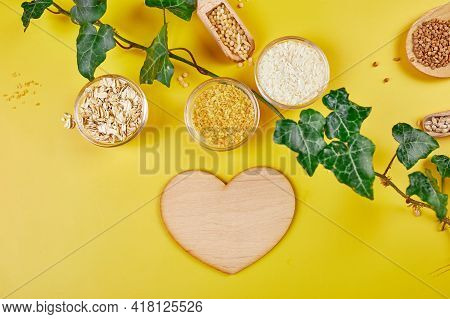 Flat Lay Of Set Of Heap Various Grains And Cereals With Greens Leaves On Yellow Background