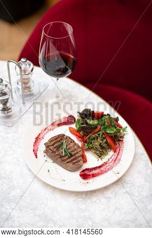 Entrecote Beef Grilled Steak Meat With Rosemary Branch, Pepper, Salt And Glass Of Red Wine In Restau