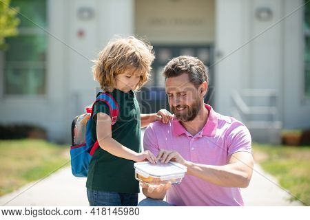 School Lunch For Kids. Father Supports And Motivates Son. Schoolboy And Parent In Shirt Holding Lunc