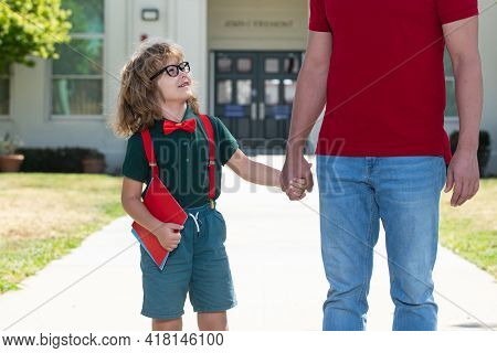 Portrait Of Happy Nerd Pupil Holding Teachers Hand. American Father And Son Walking Trough School Pa