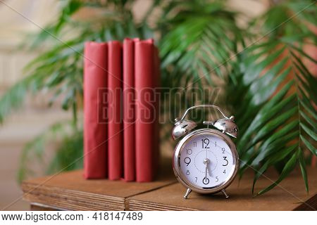 Red Stylish Photo Albums Stnding Near Clock And Houseplant On Table.