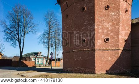 Street of Suzdal, Close up detail of red tower of Saint Euthymius monastery, residential russian small wooden traditional house across road in sunny day in spring middle april, Golden Ring of Russia