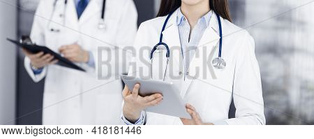 Unknown Woman Doctor Iusing Tablet Computer In Her Hands, While Standing In Clinic. Medicine Concept