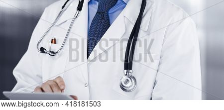 Unknown Male Doctor Iusing Tablet Computer In His Hands, While Standing In Clinic. Medicine Concept 