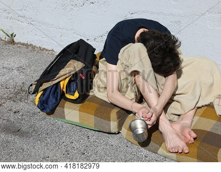 Very Poor Young Beggar While Asking For Alms From Passers-by On The Street Sidewalk Of The Metropoli