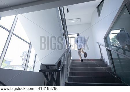 Senior african american male doctor wearing lab coat running up stairs in hospital. medical professional at work.