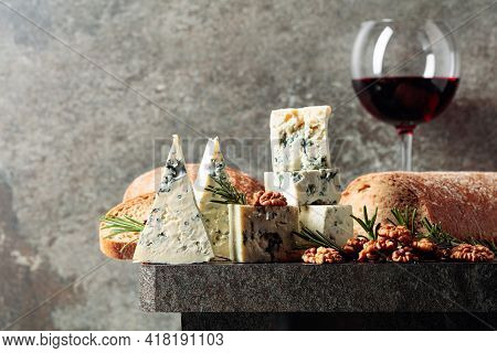 Blue Cheese And Red Wine On An Old Stone Table. Cheese With Walnuts, Bread, And Rosemary. Copy Space