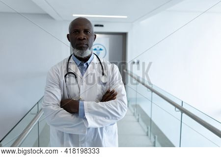 Portrait of african american male doctor standing in hospital corridor with arms crossed. medicine, health and healthcare services.