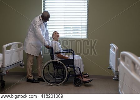 Diverse male doctor and female patient sitting on wheelchair smiling to each other. medicine, health and healthcare services.