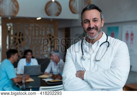 Portrait of smiling caucasian male doctor, with colleagues in discussion in the background. medicine, health and healthcare services.