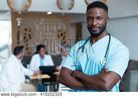 Portrait of african american male doctor smiling, with colleagues in discussion in the background. medicine, health and healthcare services.