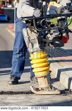 A Road Worker Repairs A Lane On The Road Using A Petrol Vibratory Rammer On A Sunny Day.
