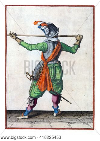 A soldier, full-length, seen from the back, carrying a spear (lance) with both hands horizontally at nose level, his right hand at the base of the weapon, his face turned to the right
