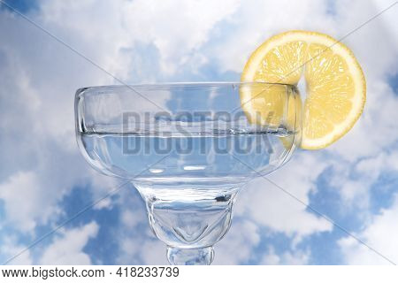 Coupe Cocktail Glass With A Lemon Wagon Wheel Garnish Against Cloudy Sky.