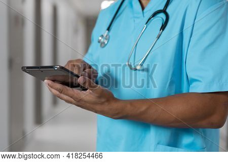 Midsection of mixes race male doctor standing in corridor using tablet. medicine, health and healthcare services.