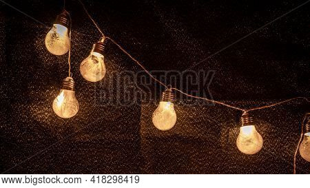 Decorative String Of Light Bulbs Containing Tiny White Featers Against A Dark Glitter Background